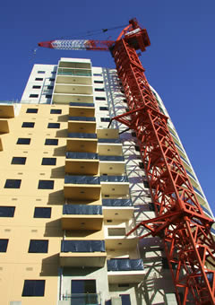 Beige high rise condo building with red crane in front.